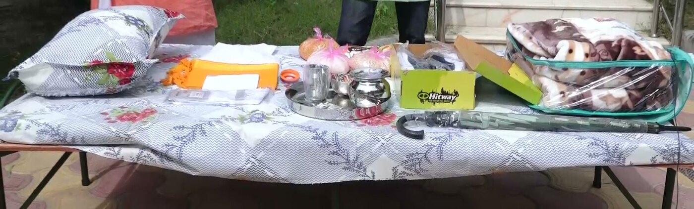 The shayya daan set laid out on the bed outside the temple in Vrindavan: pillow, sheets, folded cloths, five utensils on a steel tray, an umbrella, shoes, a blanket and the five foods